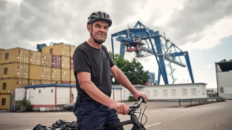 JobRadler steht am Containerhafen und blickt selbstbewusst in die Kamera JobRadler steht am Containerhafen und blickt selbstbewusst in die Kamera
